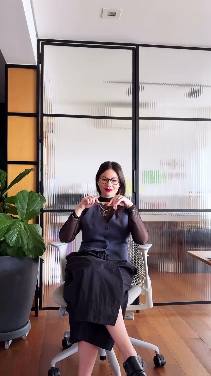 Camila Teixeira sentada em seu escritório, segurando os óculos com expressão confiante