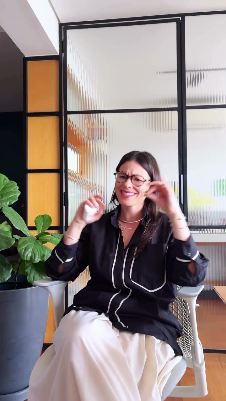 Camila Teixeira rindo enquanto ajusta os óculos, em seu escritório